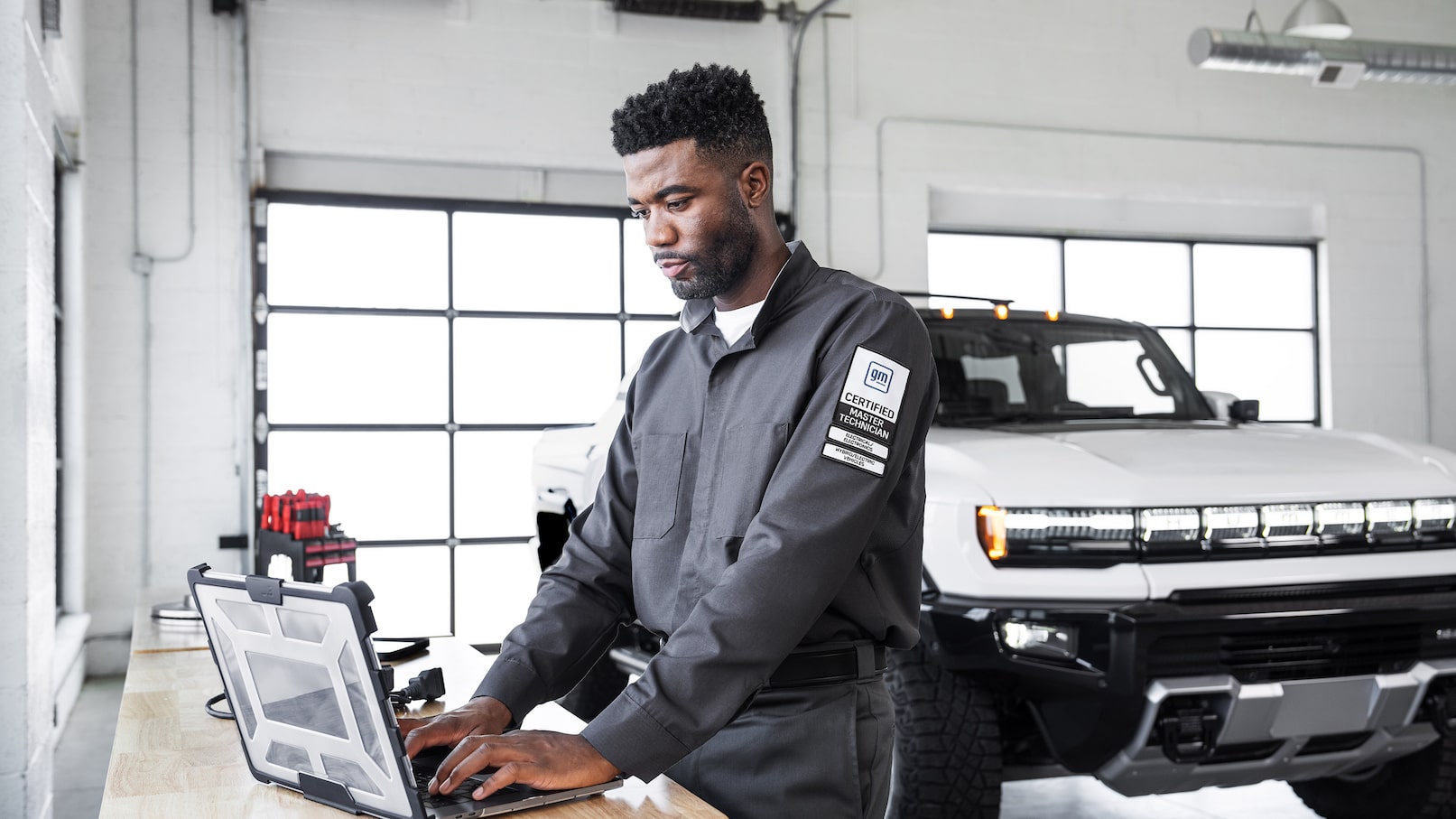Buick/GMC technician inspecting the front tire of a silver SUV in a dealership service bay