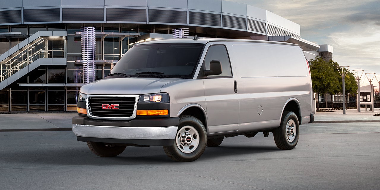 Front Three-Quarters View of the GMC Commercial Savana Cargo Van Parked in Front of a Large Building