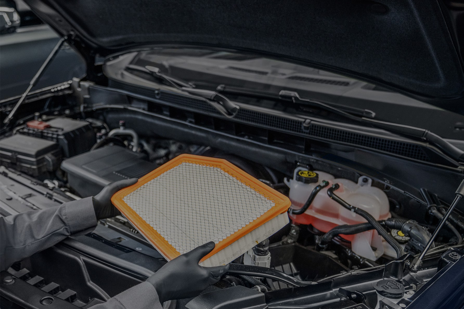A Technician Replacing the Filter Under the Hood of a Vehicle.