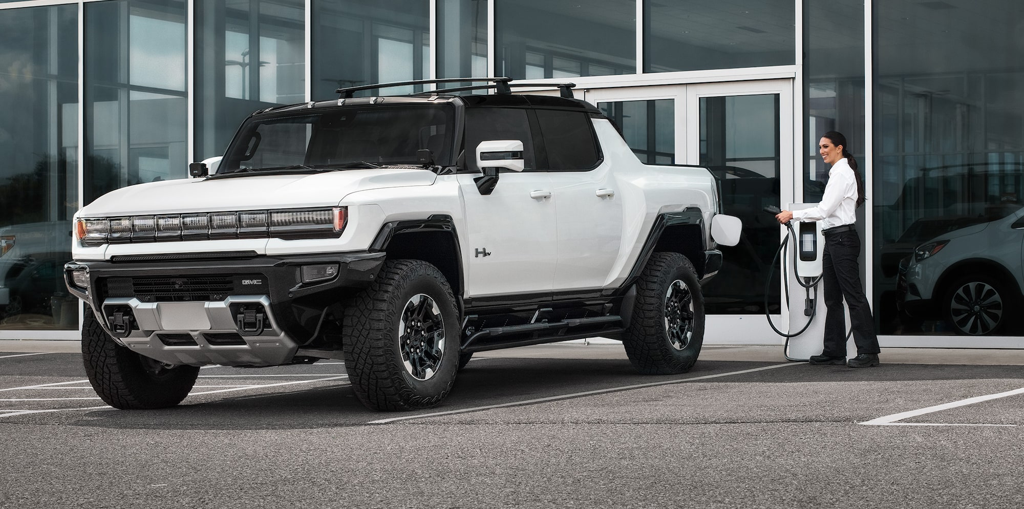 A White Hummer Pickup Truck Parked in Front of a Building with a Person Walking Up to It.