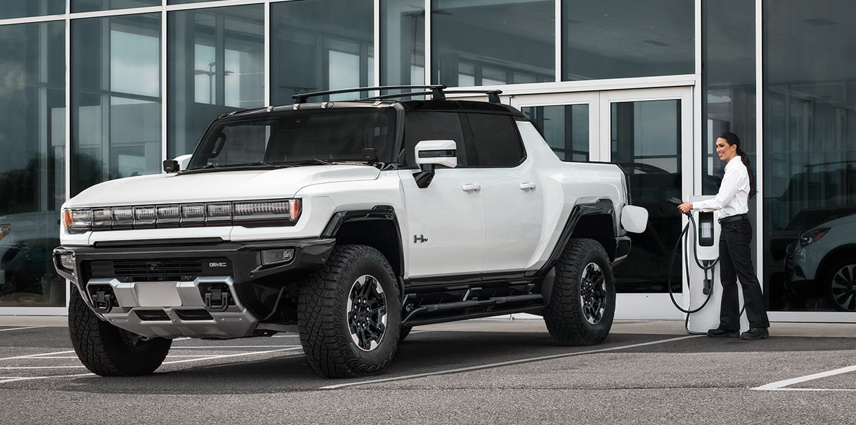A White Hummer Pickup Truck Parked in Front of a Building with a Person Walking Up to It.