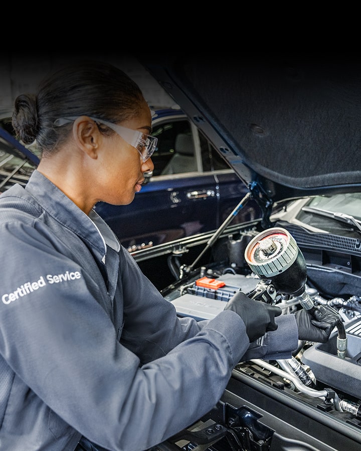 A Woman Technician Working Under the Hood of a Vehicle.
