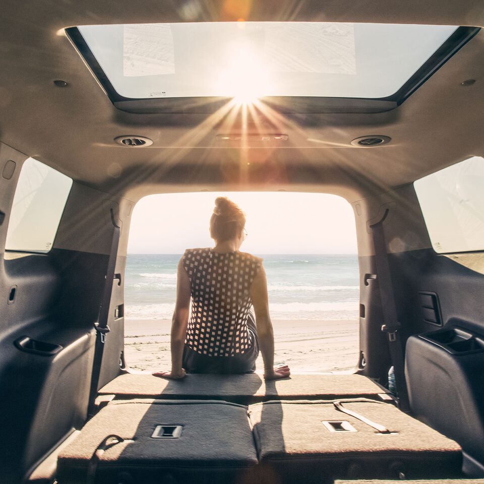 A Woman on the Beach Sitting in the Trunk of Her GMC Vehicle