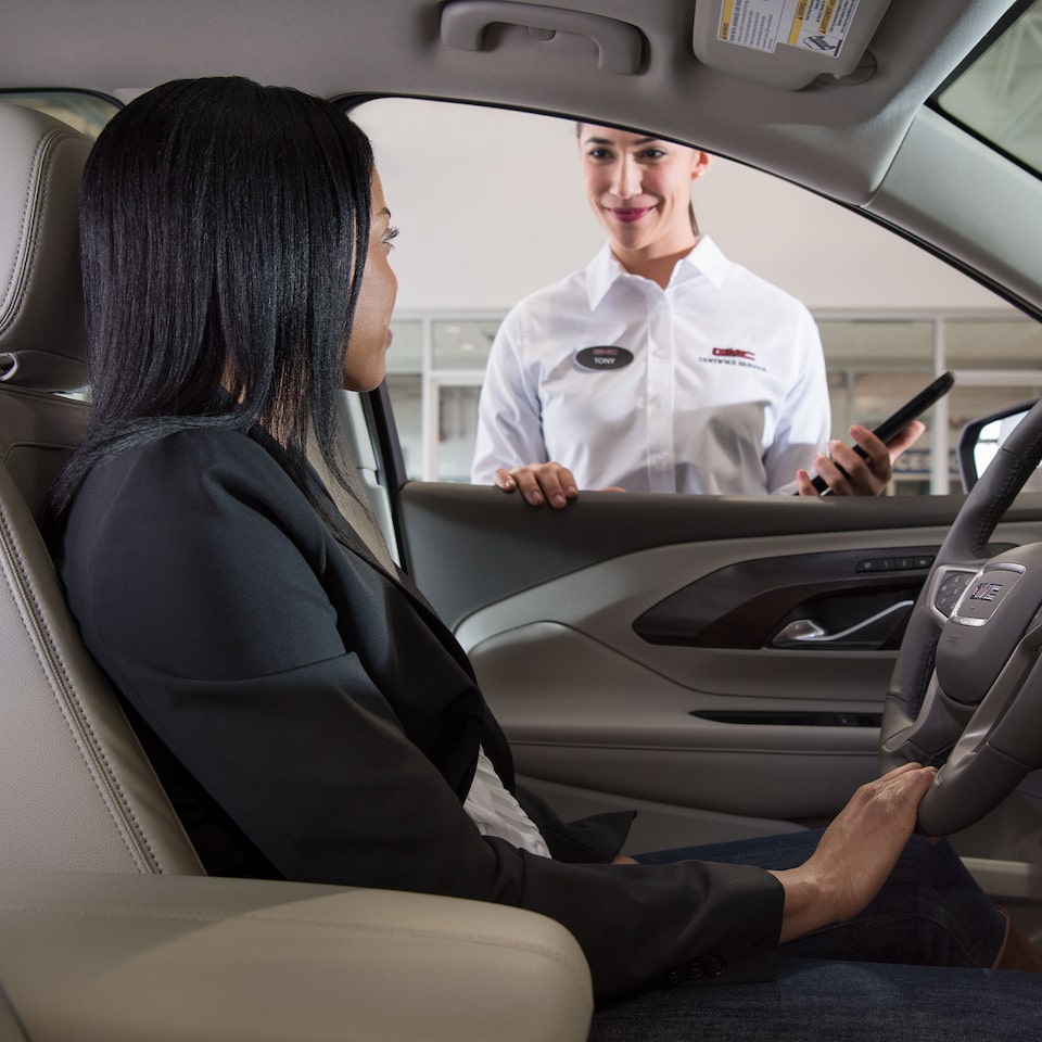 A GMC Certified Service Worker Assisting a Customer as She Sits in her GMC Vehicle