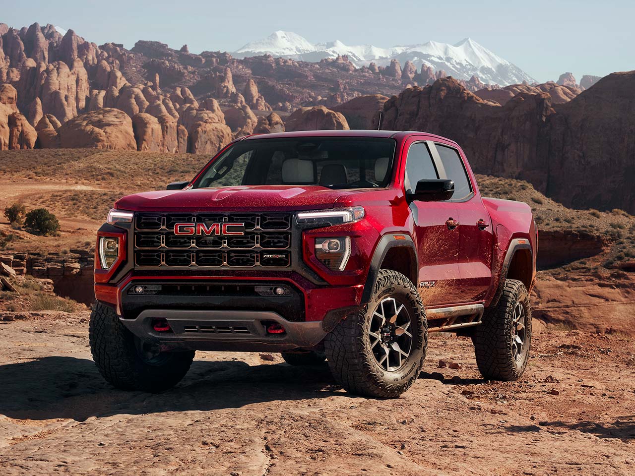 A Red GMC Canyon AT4X Truck on Rocky Desert Terrain with Rock Formations and Mountains