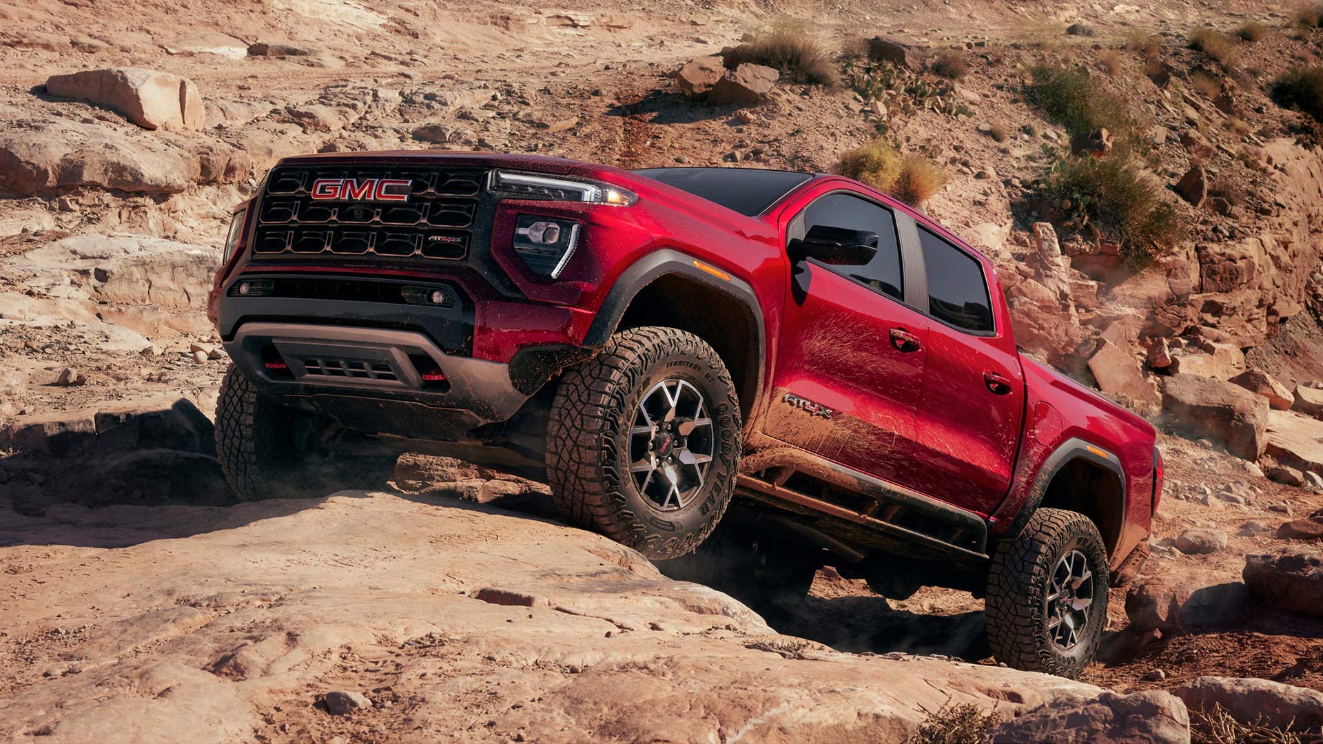 A Red GMC Canyon AT4X Pickup Truck Navigating Rocky Off-Road Terrain in a Desert Landscape