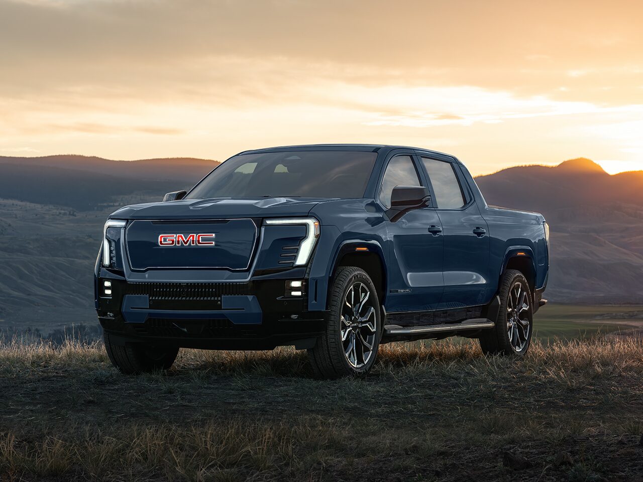 Front Three-Quarters View of the GMC Sierra EV Pickup Truck Parked in a Valley at Sunset