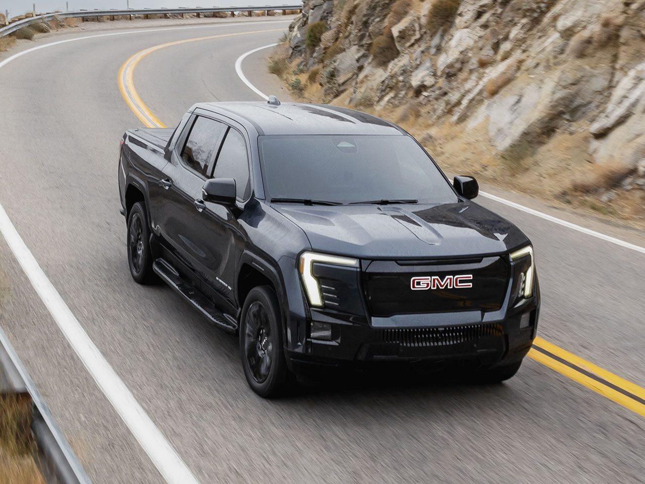 Front Three-Quarters View of the GMC Sierra EV Pickup Truck Parked in a Valley at Sunset