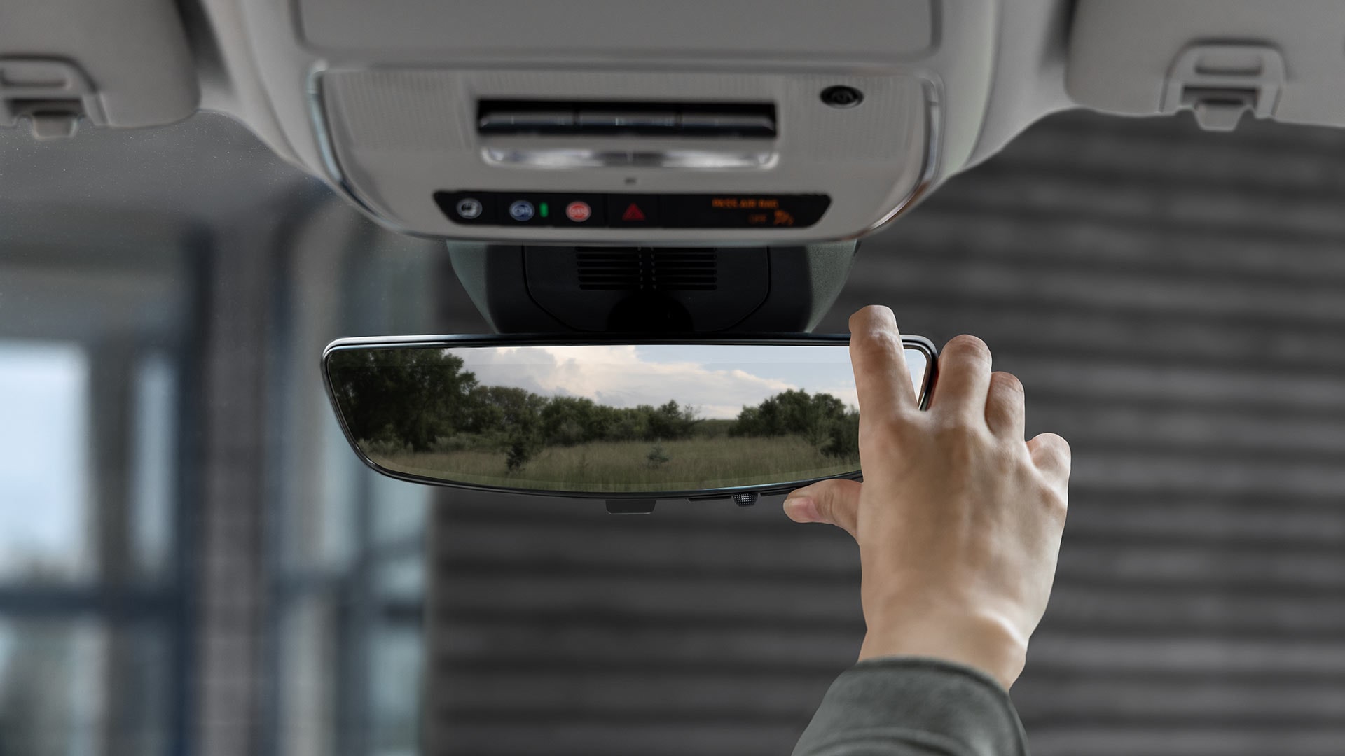A Hand Adjusting the Rearview Mirror inside a Car Showing a Field Reflected