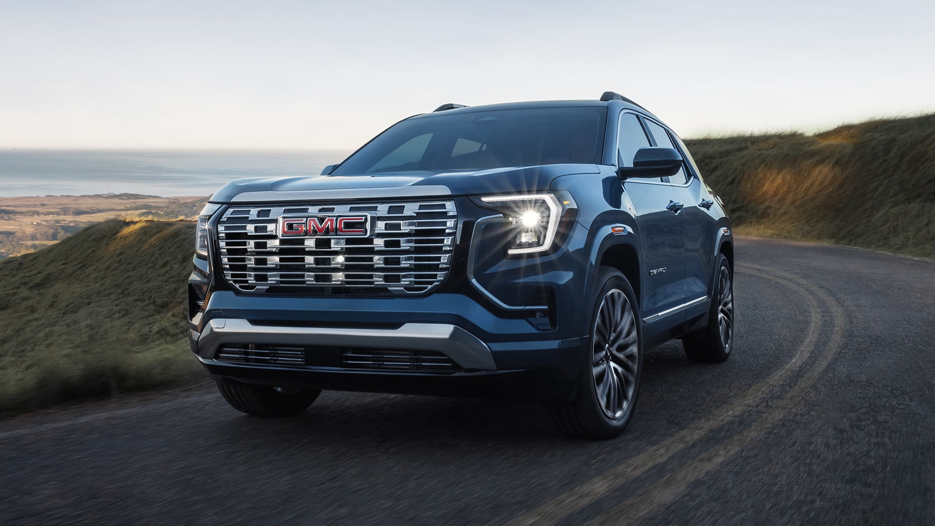 A Dark Blue GMC Terrain SUV Driving on a Winding Road with a Hazy Landscape