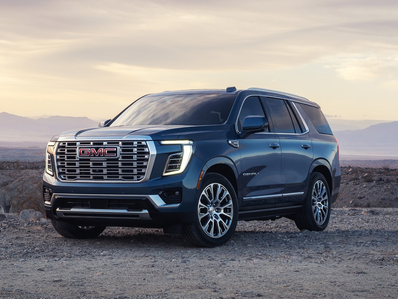 Front Three-quarters View of the GMC Yukon SUV Parked in the Desert at Sunset with Mountains in the Distance