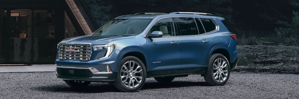 Front Three-quarter View of a Blue GMC Acadia Denali Parked in the Woods in Front of the Beautiful Cabin