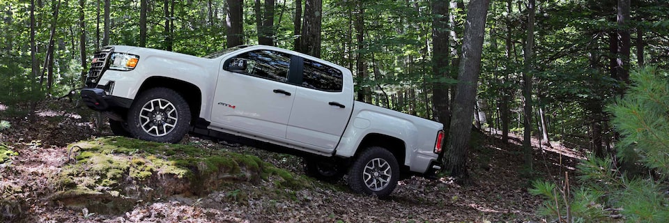 Profile View of a GMC Canyon AT4 Off-Road Truck Driving Over Hilly Terrain in the Forest