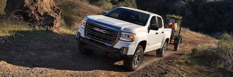 Front Three-Quarter View of a White GMC Canyon AT4 Off-Road Truck Towing a Trailer with a Dirt Bike