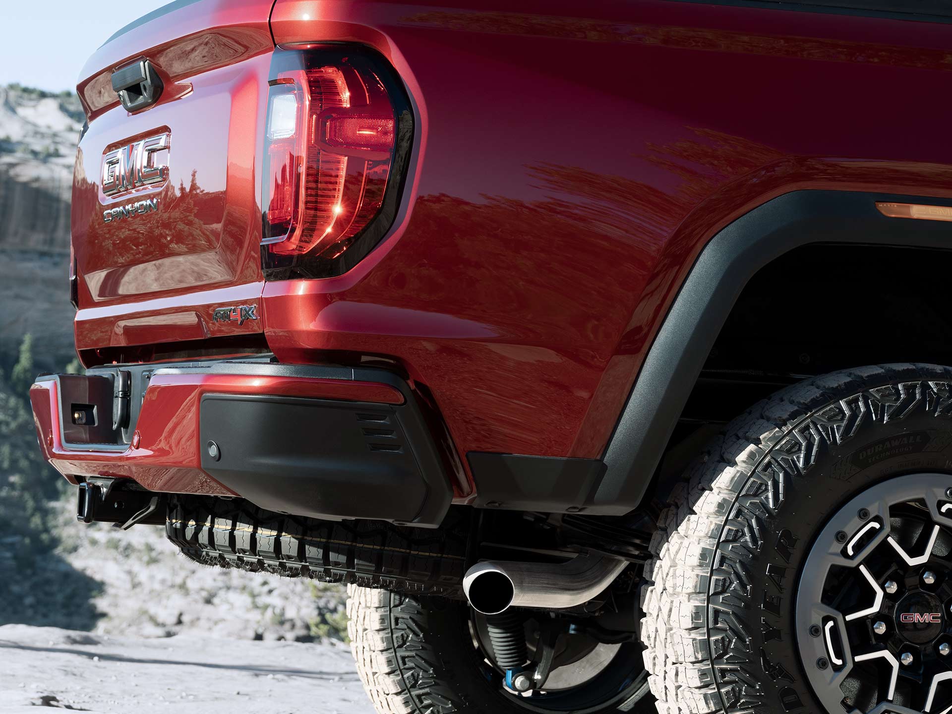 A Close-Up of the Rear Taillight and Bumper of a Red GMC Canyon AT4X Pickup Truck in a Rugged Outdoor Setting