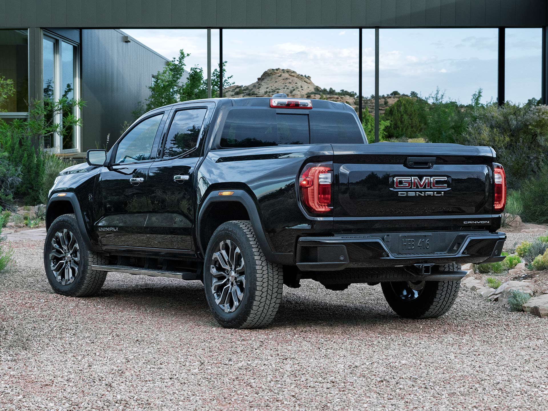 The Rear View of a Black GMC Canyon Denali Pickup Truck Parked on a Gravel Driveway in Front of a Modern House
