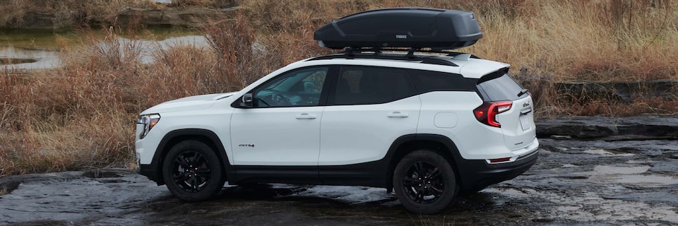 A Overlooking Shot of a White GMC Terrain Parked Off Road On Dark Rocks by the Water