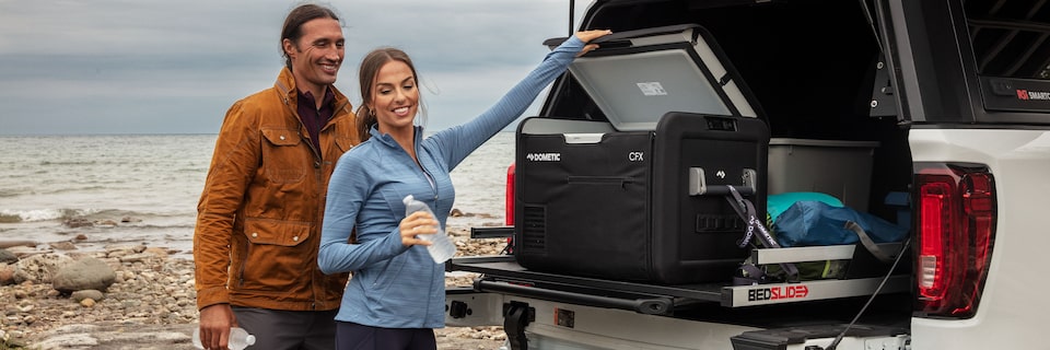 A Man and Women Off Road By the Water Opening a Cooler in the back of a GMC Vehicle