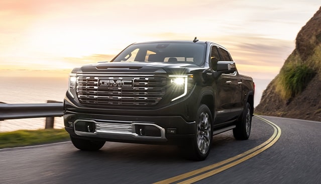 A GMC Truck Driving Down a Winding Road While the Sunsets