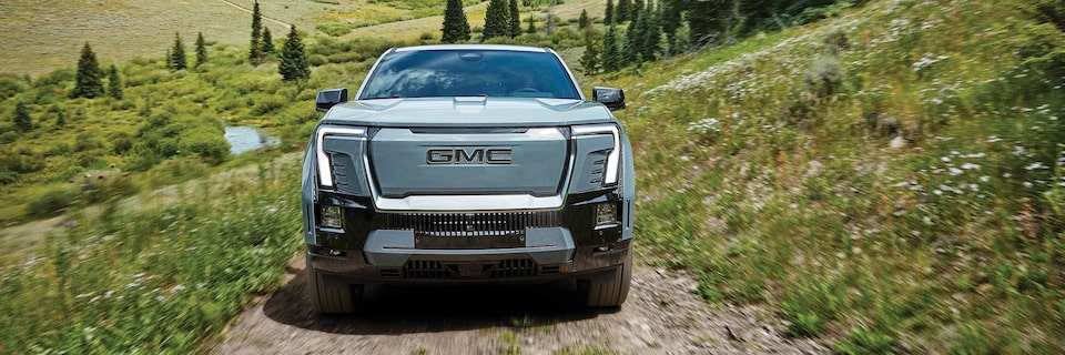 Head on View of the GMC Sierra EV Denali Truck Driving Up Grassy Hills.