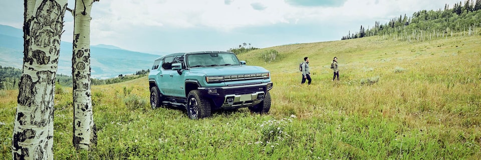 The GMC Hummer EV SUV Parked on Grassy Hills with Two People Hiking.