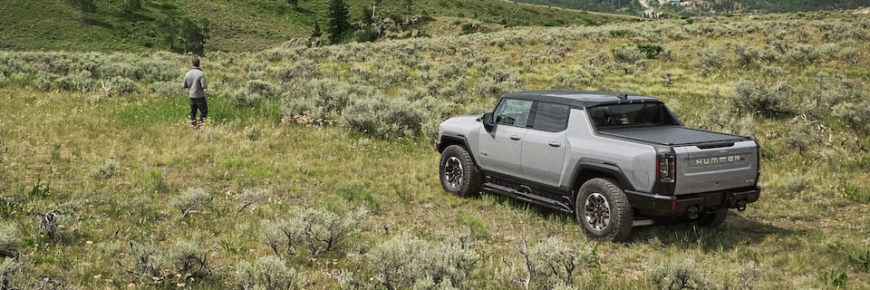 A Man Standing in a Green Meadow with his HUMMER EV Pickup Truck Parked Behind him