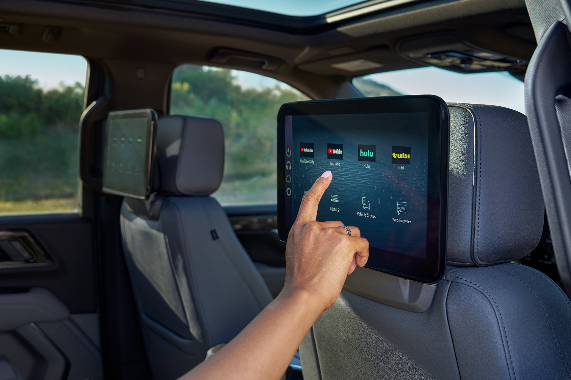 A Hand Interacting with the Rear Seat Entertainment Screen of a GMC SUV Displaying App Icons