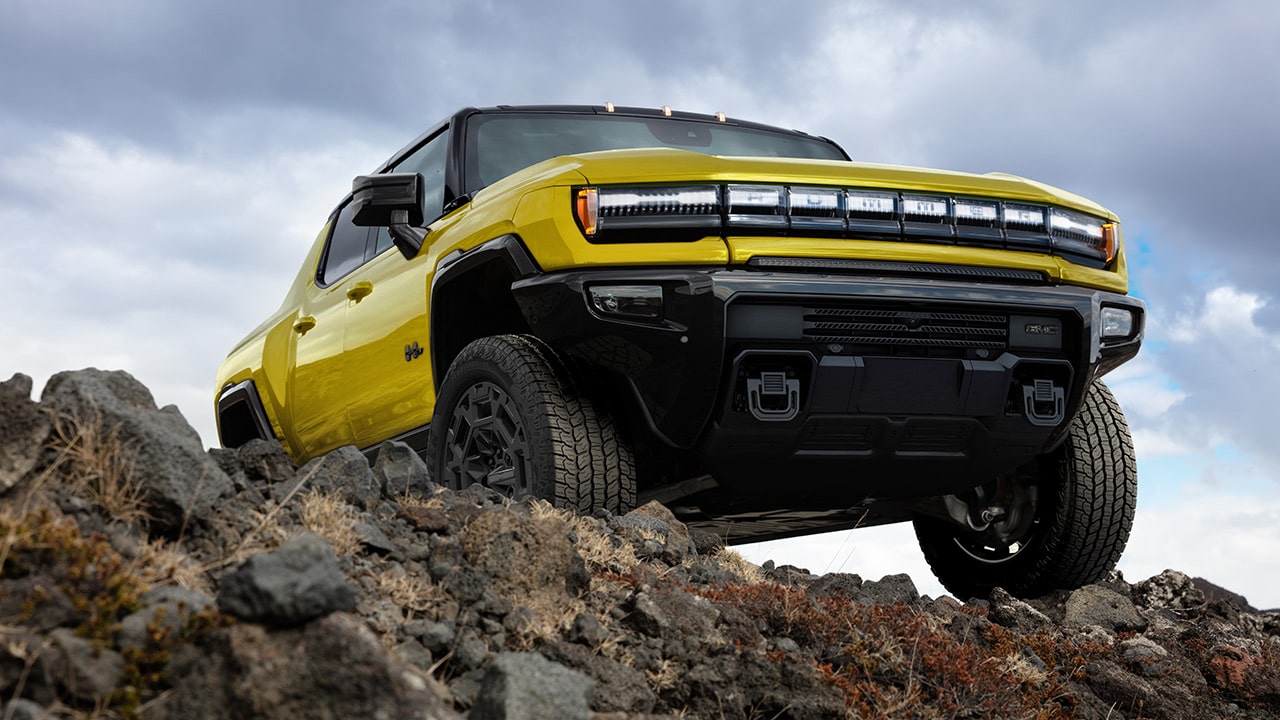 A Yellow GMC HUMMER EV Pickup Truck Navigating Rocky Terrain Under a Cloudy Sky