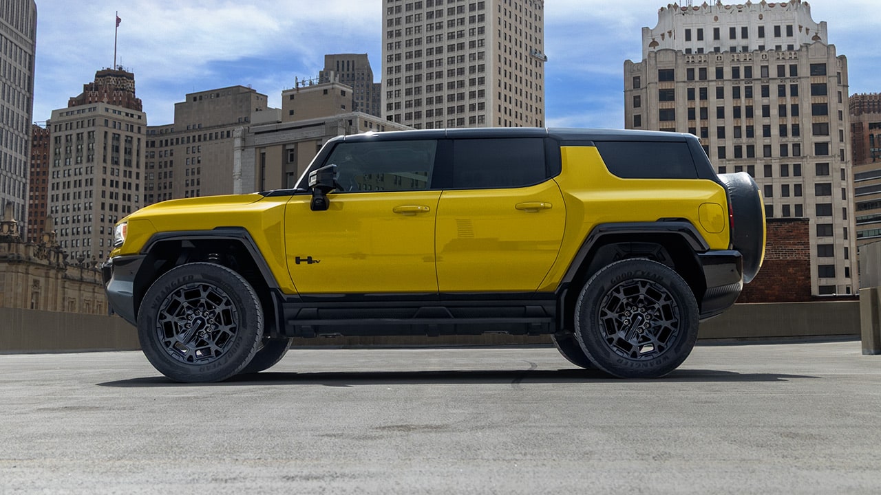 A Side Profile of a Yellow GMC HUMMER EV SUV With Black Wheels Parked in a City Landscape