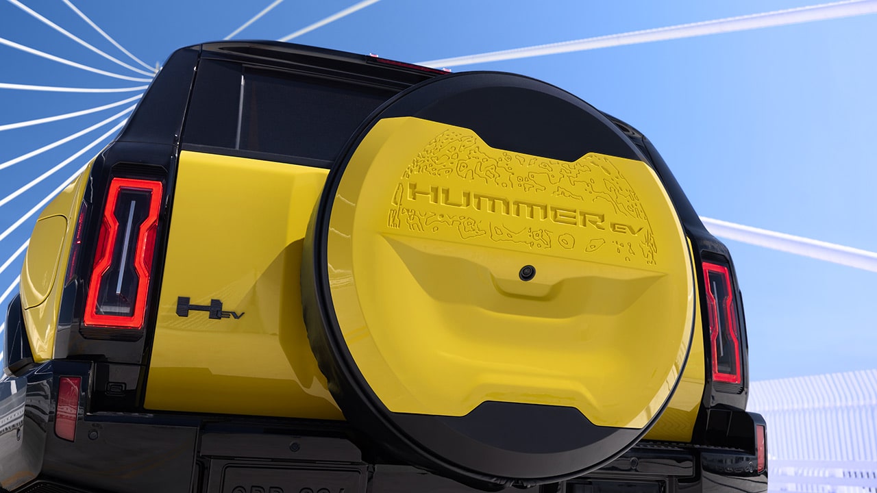 The Rear View of a Yellow GMC HUMMER EV SUV With a Spare Tire Cover Featuring a Topographical Map Design