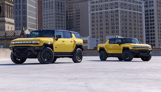 Two Yellow GMC HUMMER EV Vehicles, an SUV and a Pickup Truck, Parked in an Urban Setting