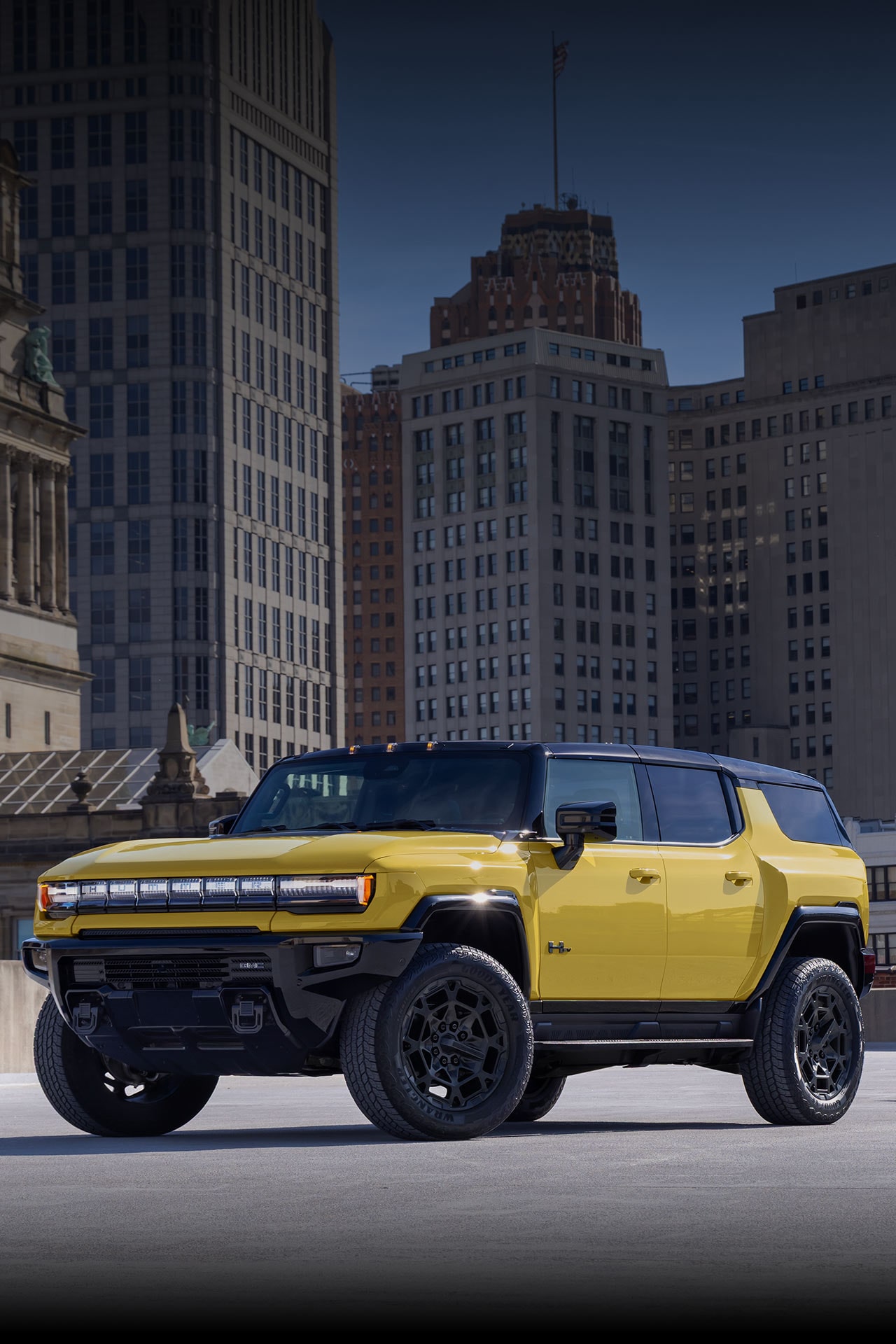 Two Yellow GMC HUMMER EV Vehicles, an SUV and a Pickup Truck, Parked in an Urban Setting