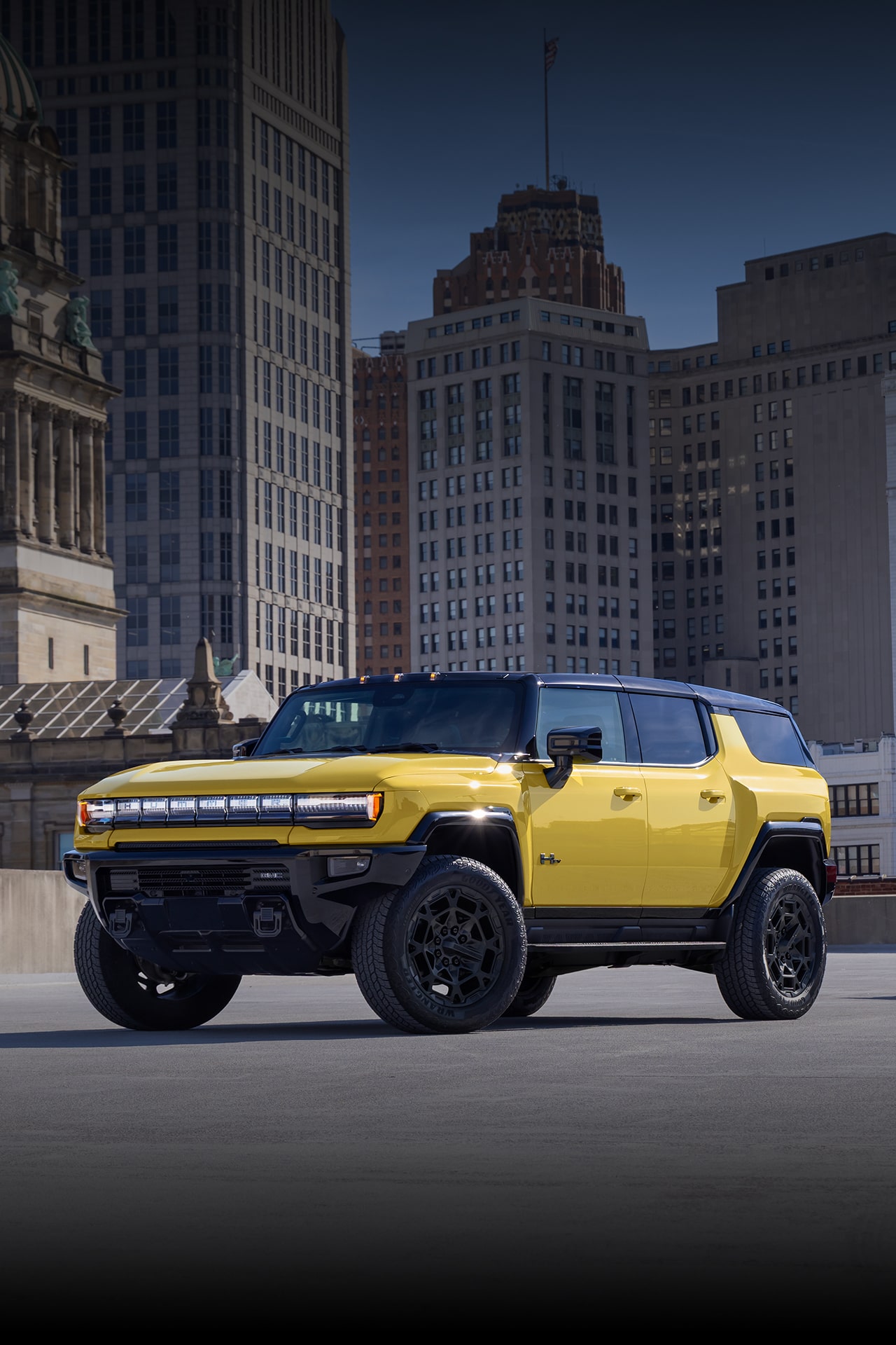 Two Yellow GMC HUMMER EV Vehicles, an SUV and a Pickup Truck, Parked in an Urban Setting