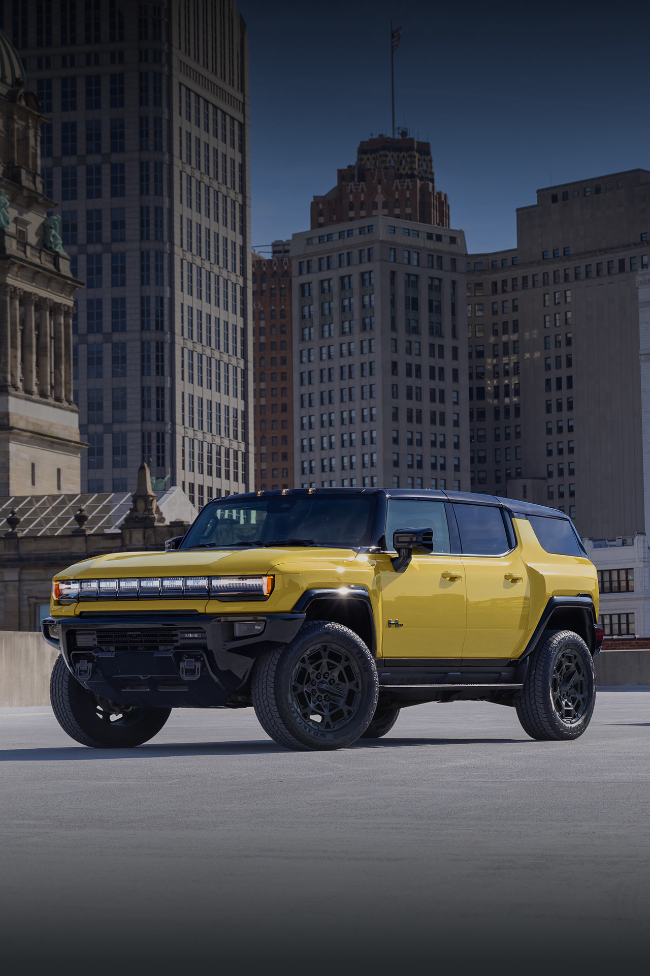 Two Yellow GMC HUMMER EV Vehicles, an SUV and a Pickup Truck, Parked in an Urban Setting