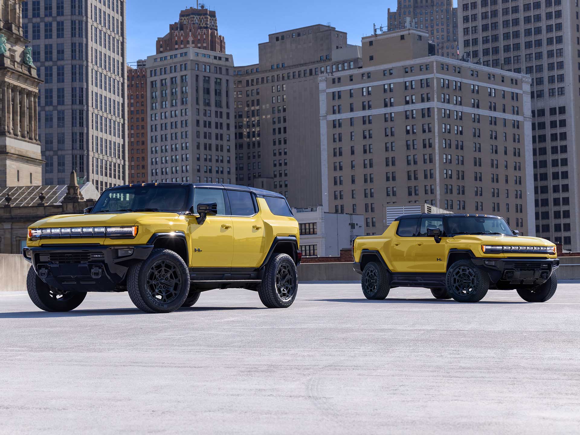 Two Yellow GMC HUMMER EV Vehicles, an SUV and a Pickup Truck, Parked in an Urban Setting