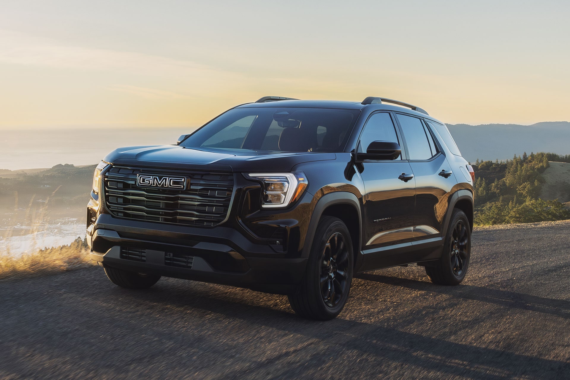 A Black GMC Acadia Driving on a Winding Road with a Sunset in the Background