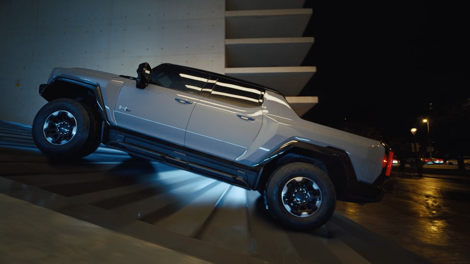 A Light Gray GMC Hummer EV Pickup Truck Driving Up a Concrete Ramp at Night