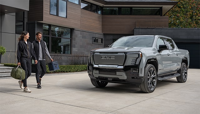 A Couple Leaving Their House and Walking to Their Sierra EV Pickup Truck Parked in the Driveway