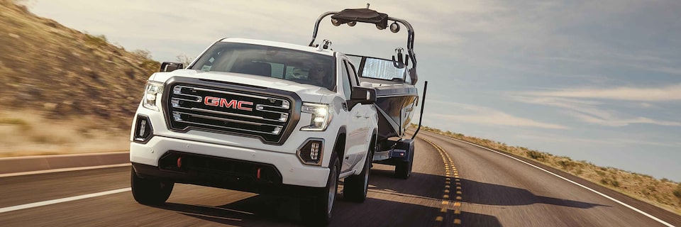 White GMC Sierra AT4 3L Duramax Diesel truck towing a boat on desert road - wide view