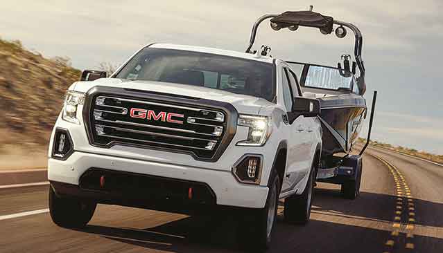 White GMC Sierra AT4 3L Duramax Diesel towing a boat on desert road - narrow view