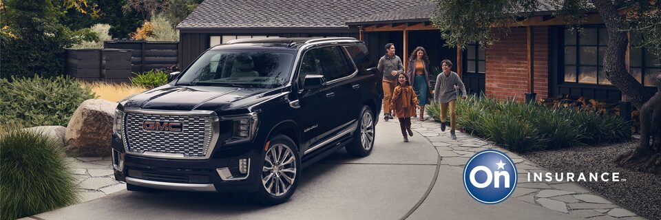 GMC Yukon Large SUV sits in the driveway while a family of four exits the house and is walking toward the vehicle. OnStar Insurance logo is in the bottom right corner of the image