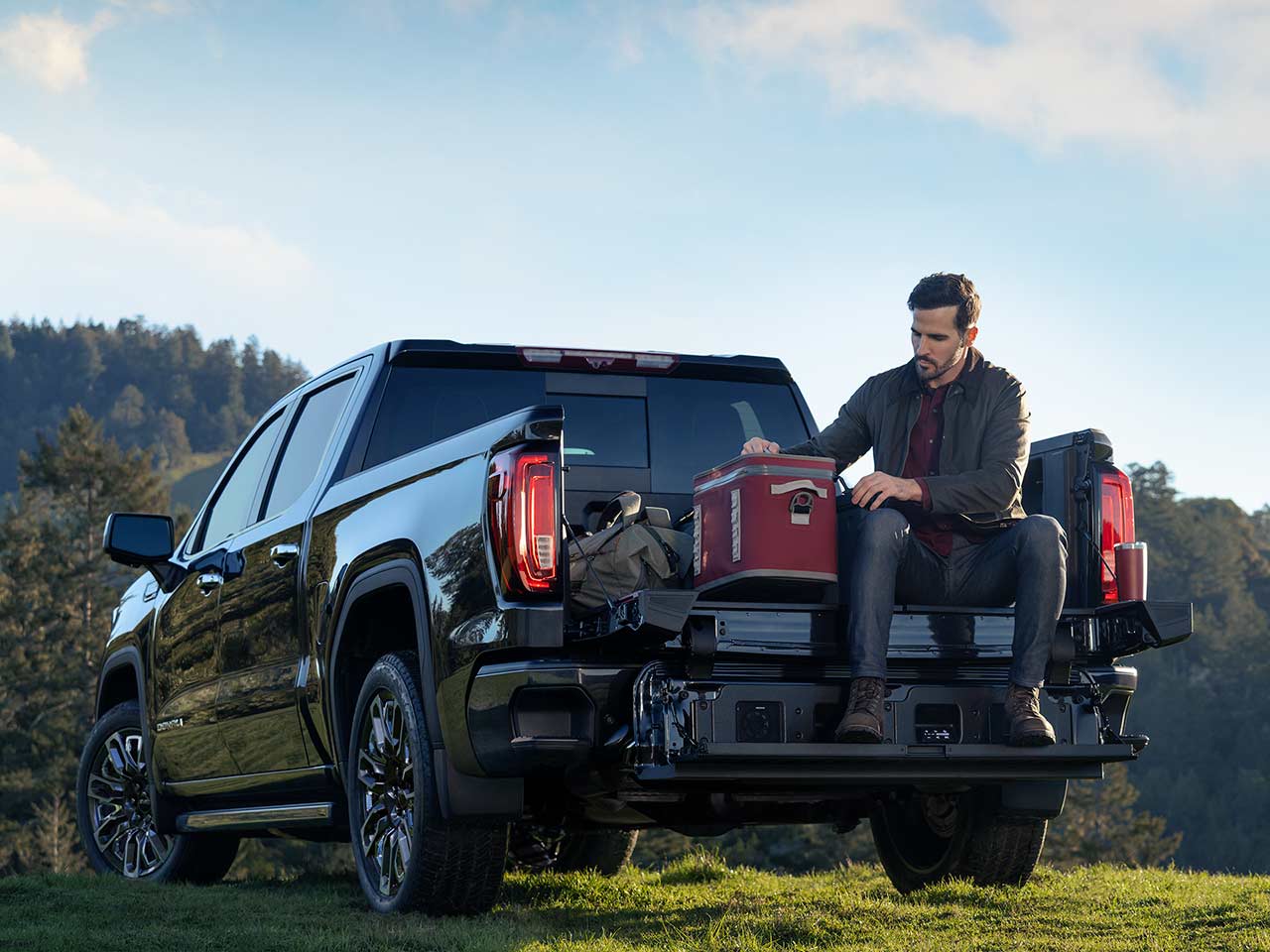The Rear Side View of a Dark GMC Sierra Denali Truck With Robust Off-Road Tires, Parked in a Desert Landscape With Snowy Mountains in the Distance