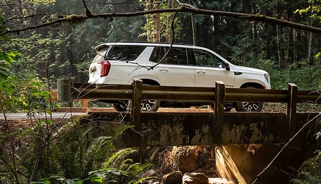 Profile View of a GMC Yukon Driving Over a Bridge in the Forrest