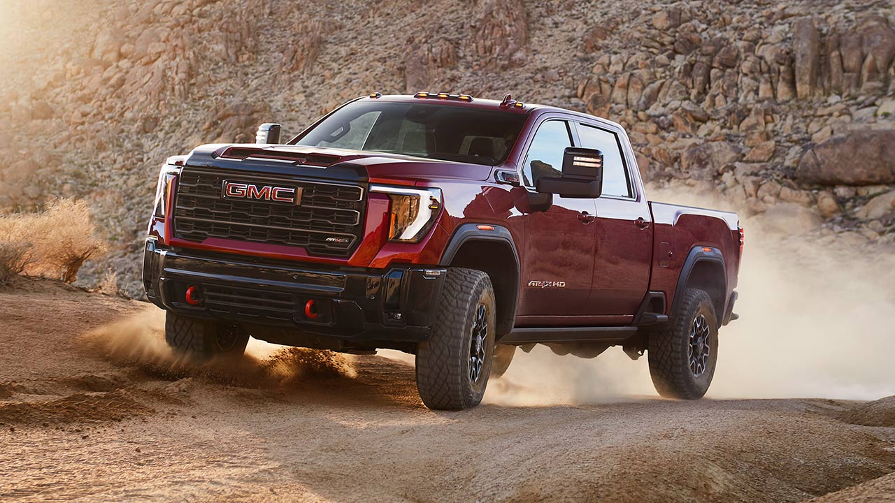 A Vibrant Red GMC Sierra AT4X Truck Kicks Up Dust as It Navigates a Rocky Off-Road Trail in a Sunlit Desert Landscape