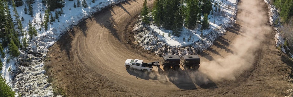 Overhead View of a White GMC Pickup Truck Making a U-Turn on a Road While Pulling Two Trailers