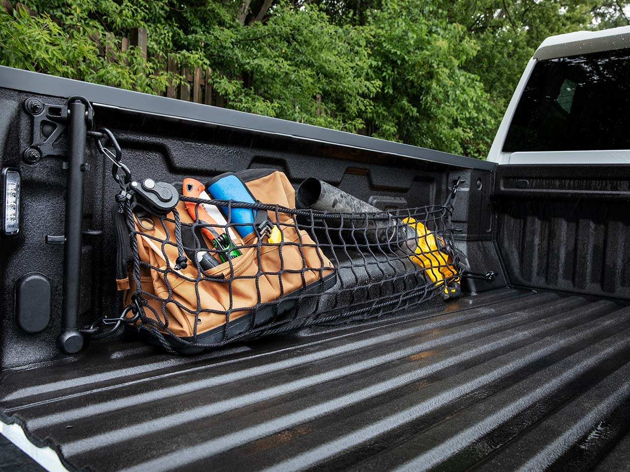 A Close-Up View of a Pickup Truck Bed with a Black Cargo Net Holding Tools and a Brown Canvas Bag