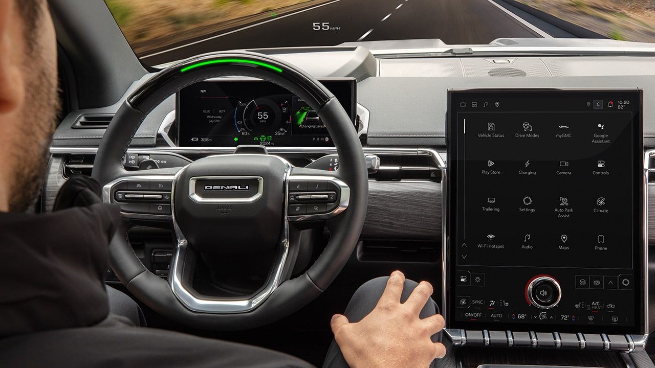 An Over the Shoulder View from a Driver of a GMC Denali Dashboard and Infotainment Screen Displaying Apps