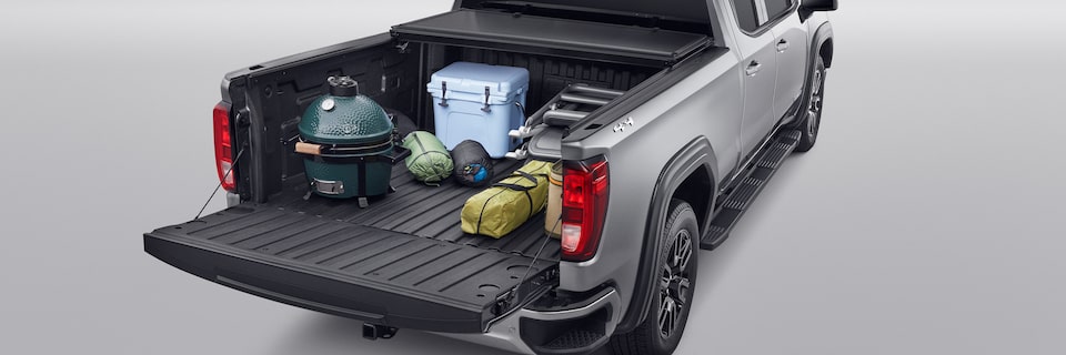 Three-Quarters Rear View of a Grey GMC Pickup Truck with a Grill, Ice Cooler, and Sleeping Bags in the Truck Bed
