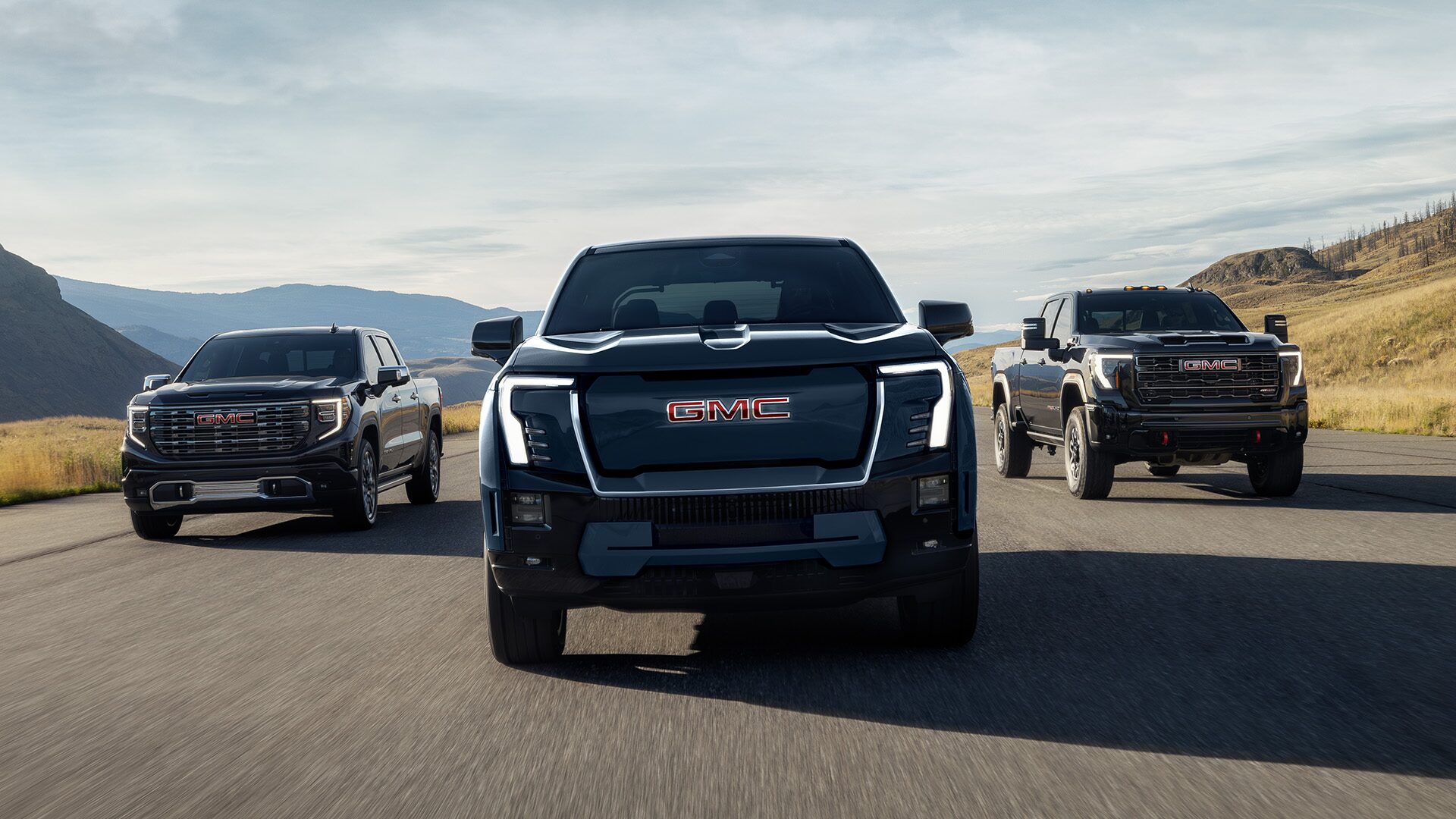 Front View of Three GMC Pickup Trucks Driving Down an Open Road