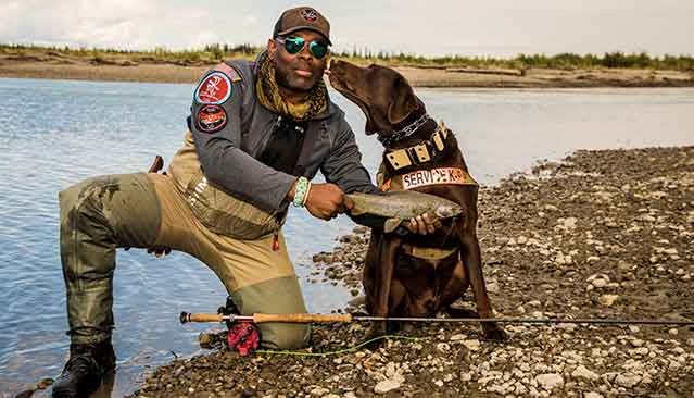 A Man and His Dog Posing for a Picture by the River as the Man Holds a Fish He Caught
